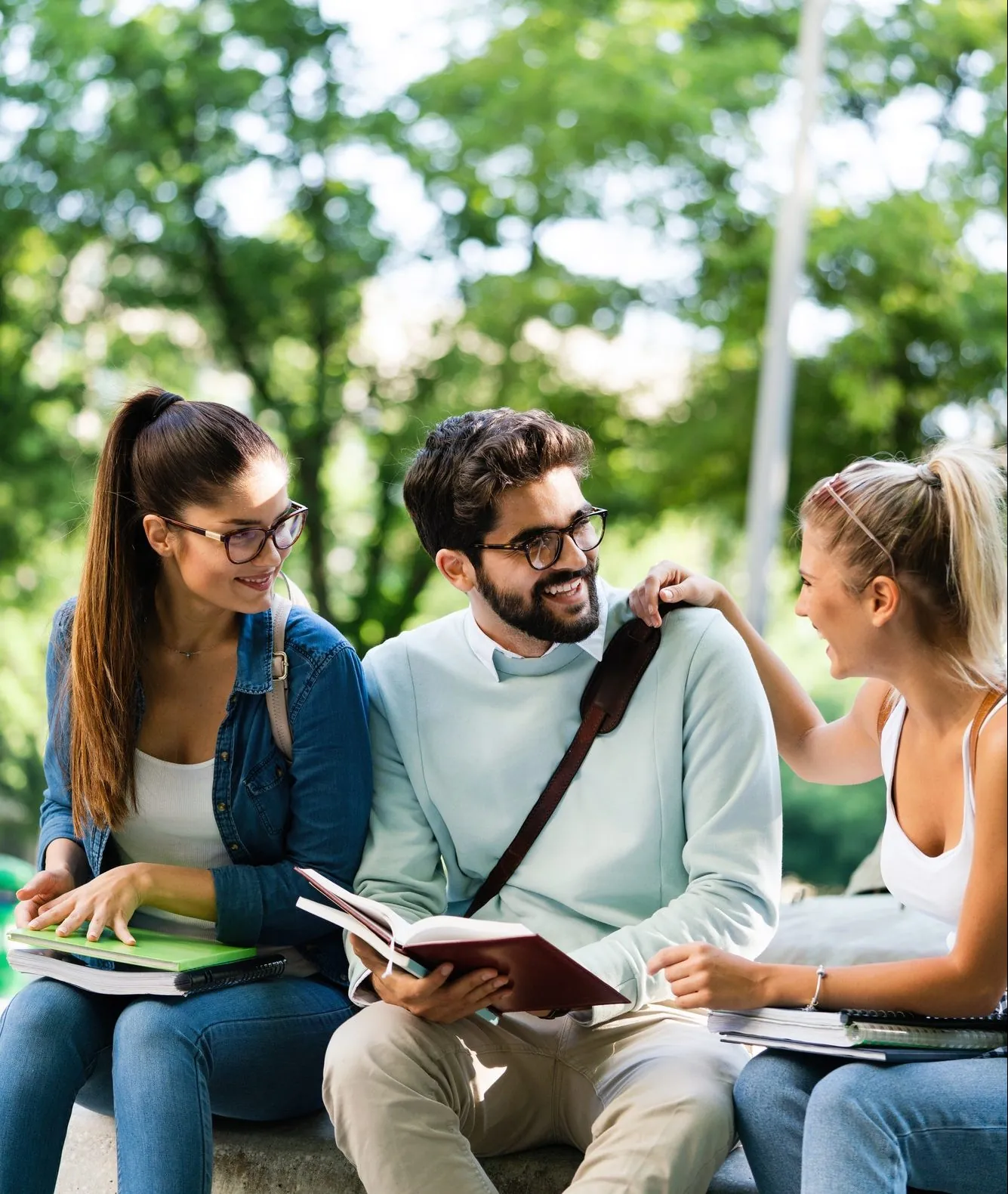 Group of students studying outdoors on campus, smiling and sharing books.