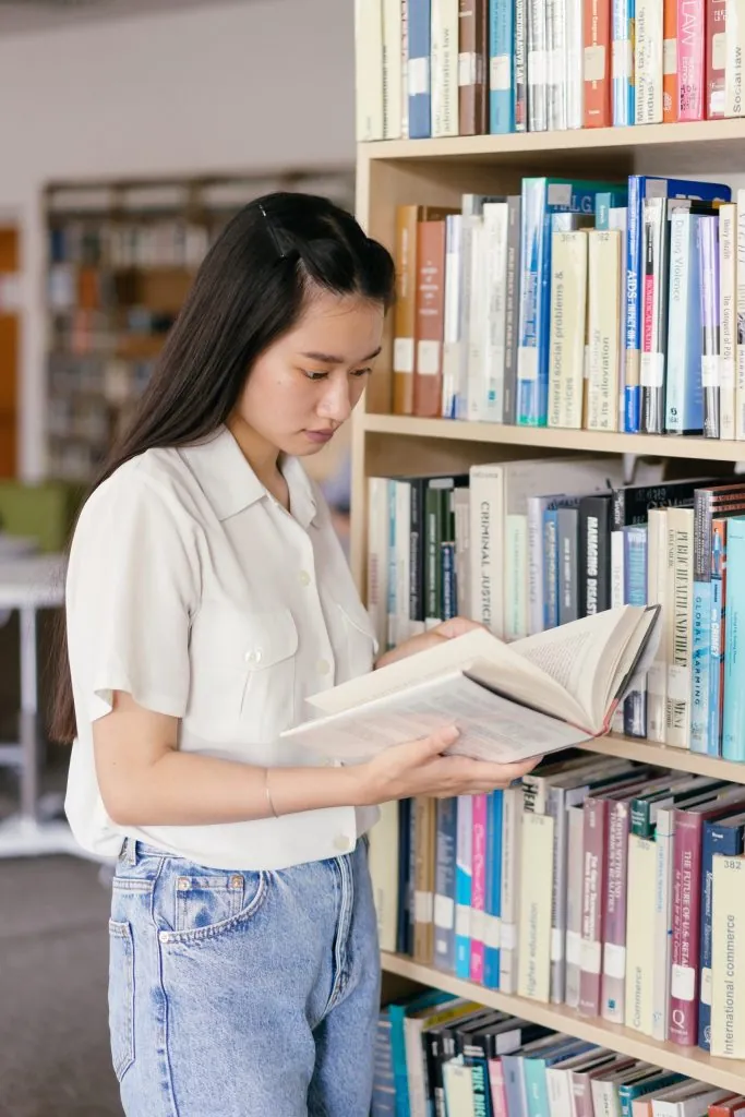 Woman reading a book in a library, related to clinical research expertise.